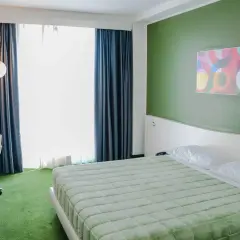 A modern hotel room with a green bedspread, green carpet, and a colorful abstract art piece on a green wall.